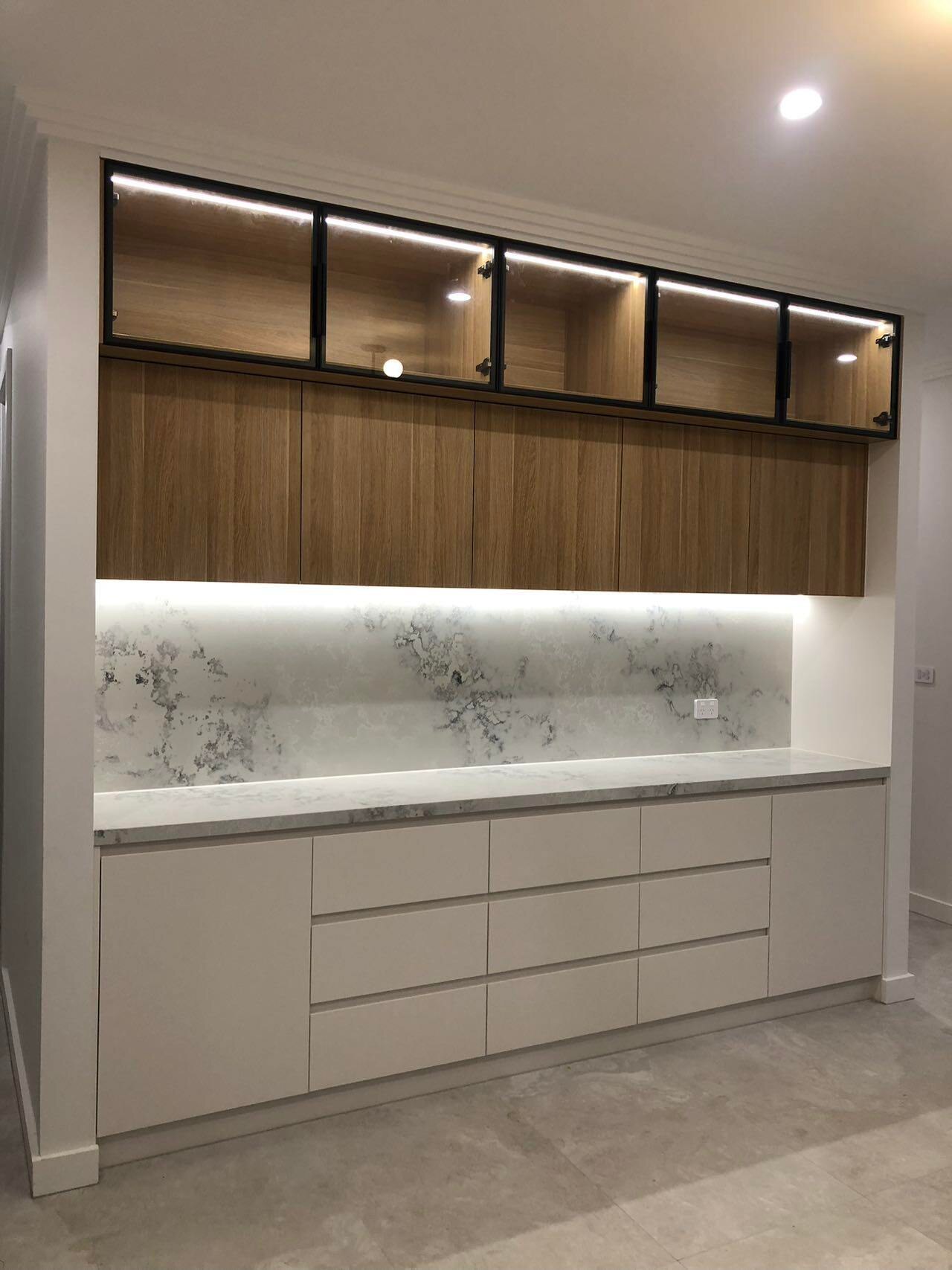 Built-in sideboard with timber overhead cupboards, black-framed glass doors and a stone benchtop