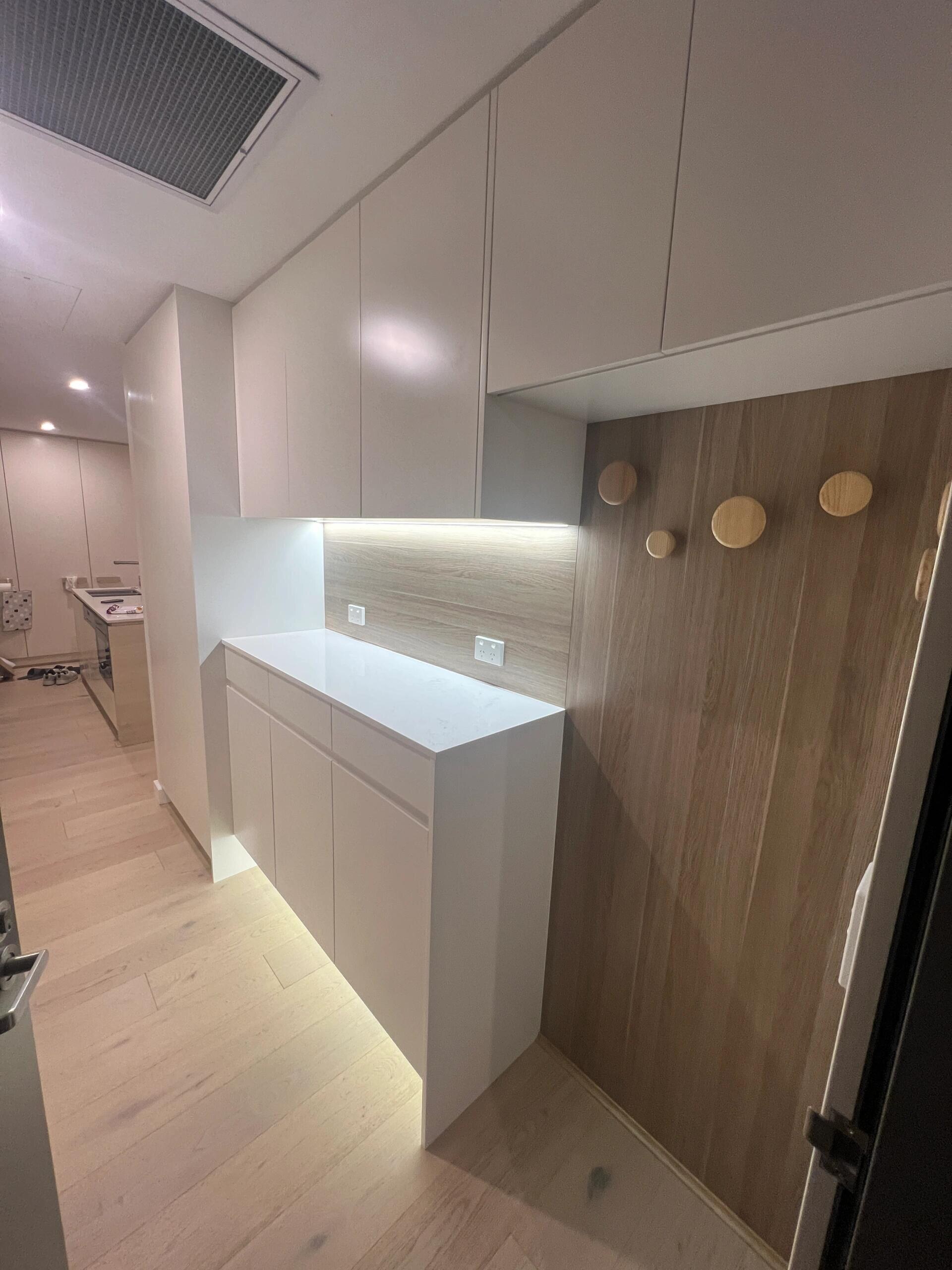 Entry with a white shoe cabinet, overhead cupboards and a timber panel wall with round coat hooks