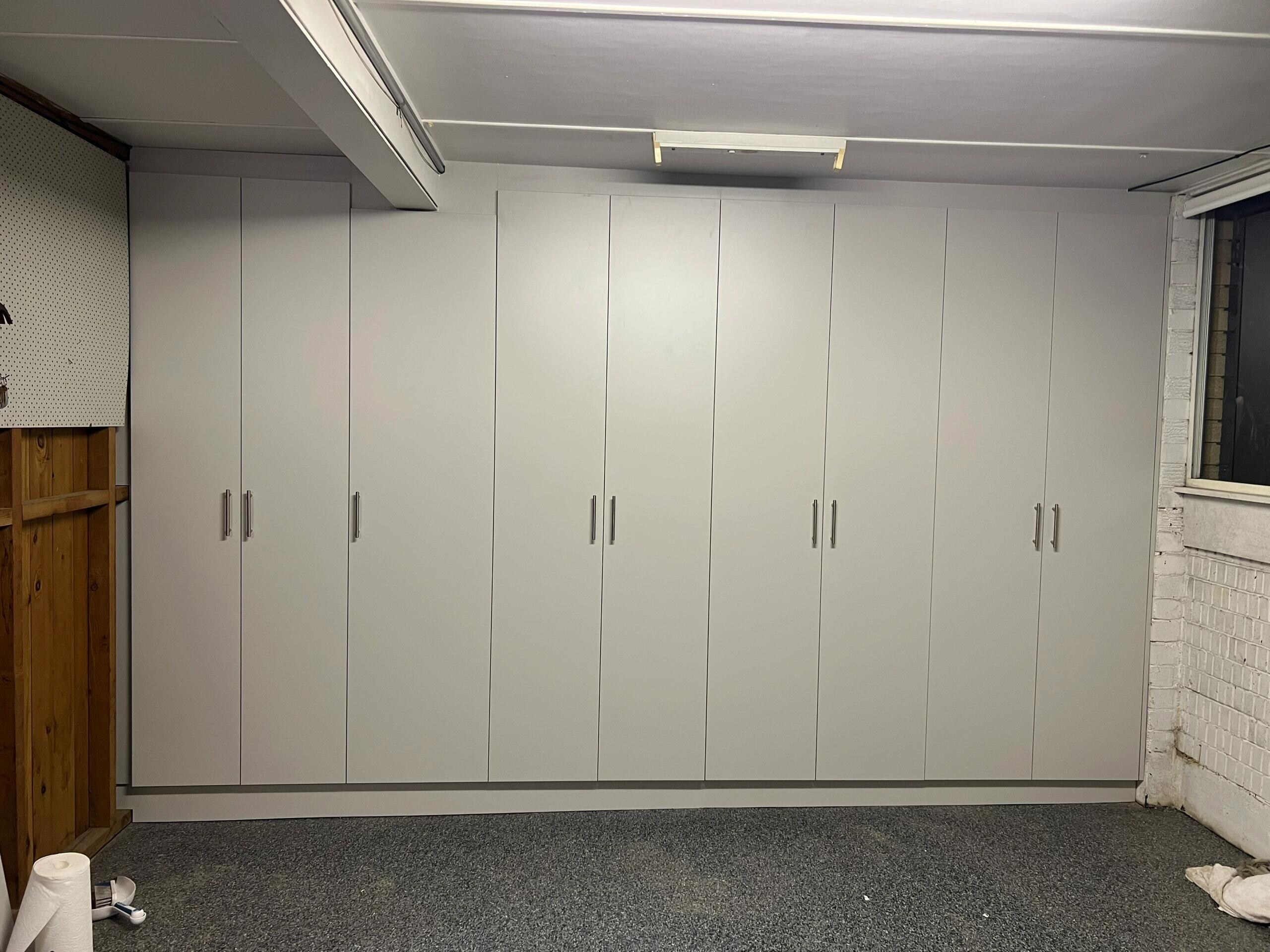 A full wall of tall white garage storage cupboards with long handles