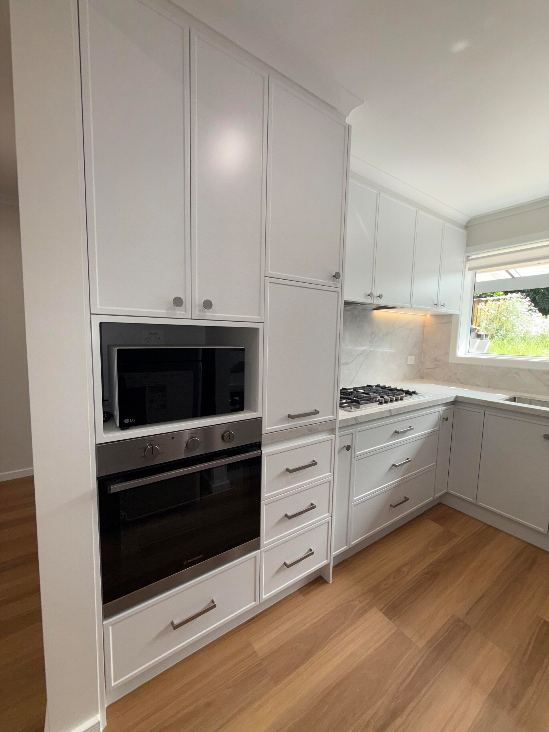 White shaker kitchen with a tall oven tower, drawers and marble-look benchtop and splashback