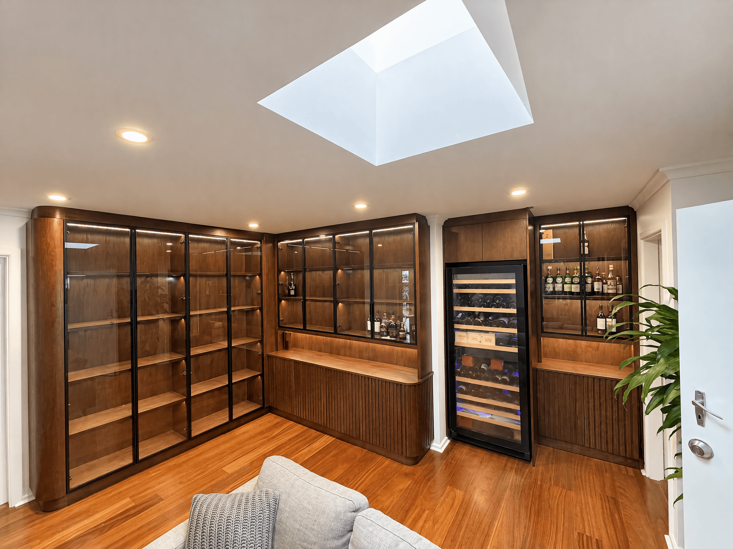 Dark timber bar wall with glass-door display cabinets, fluted lower doors and a built-in wine fridge
