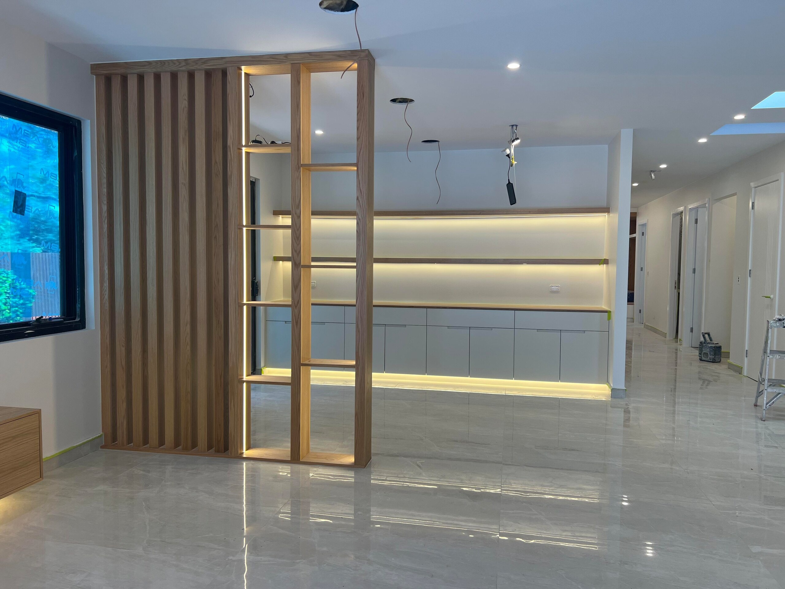 Timber slat room divider with lit open shelves, in front of a wall of low cupboards and floating shelves