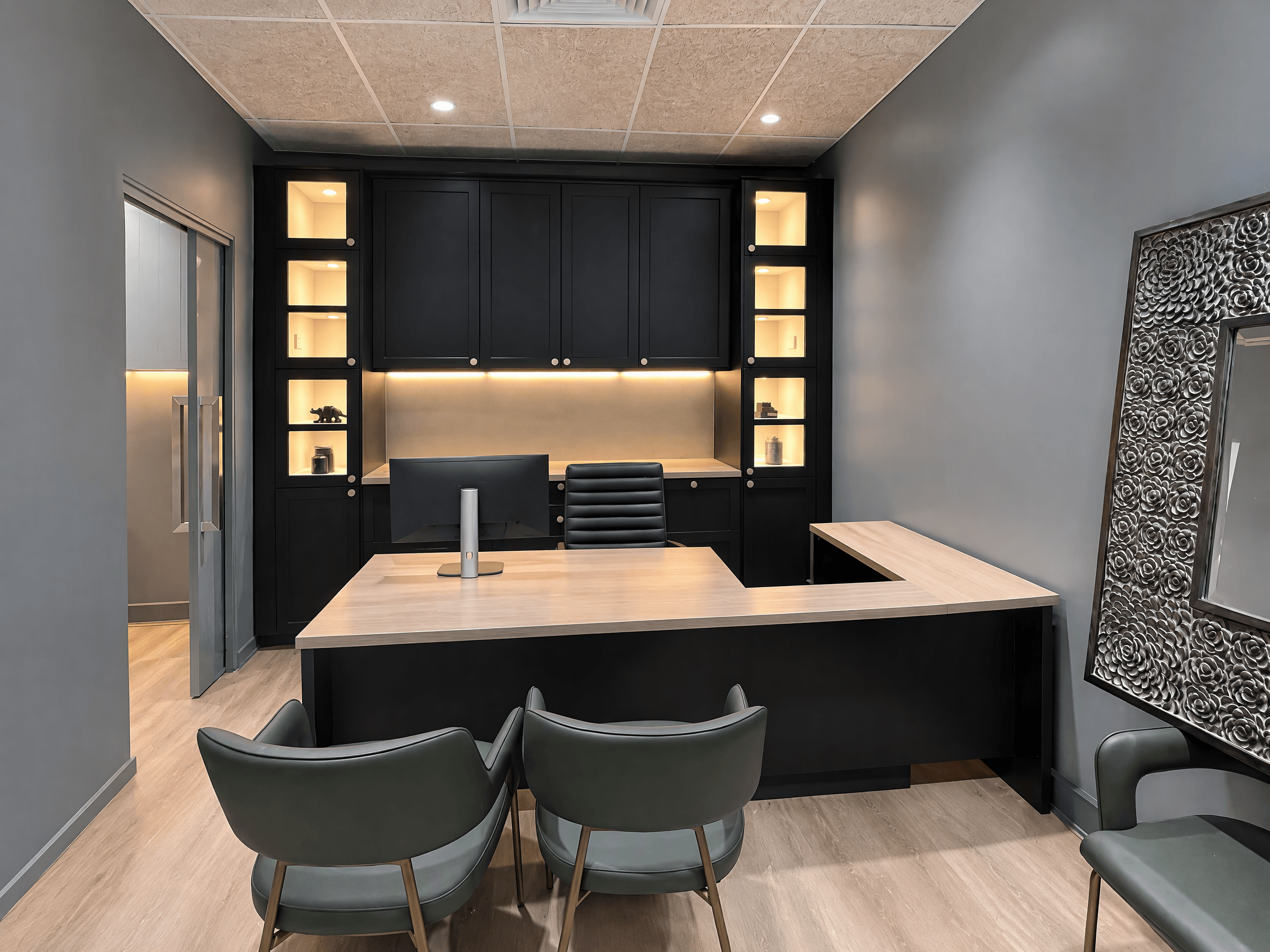 Office with a black built-in back wall of lit display niches and a timber-top L-shaped desk