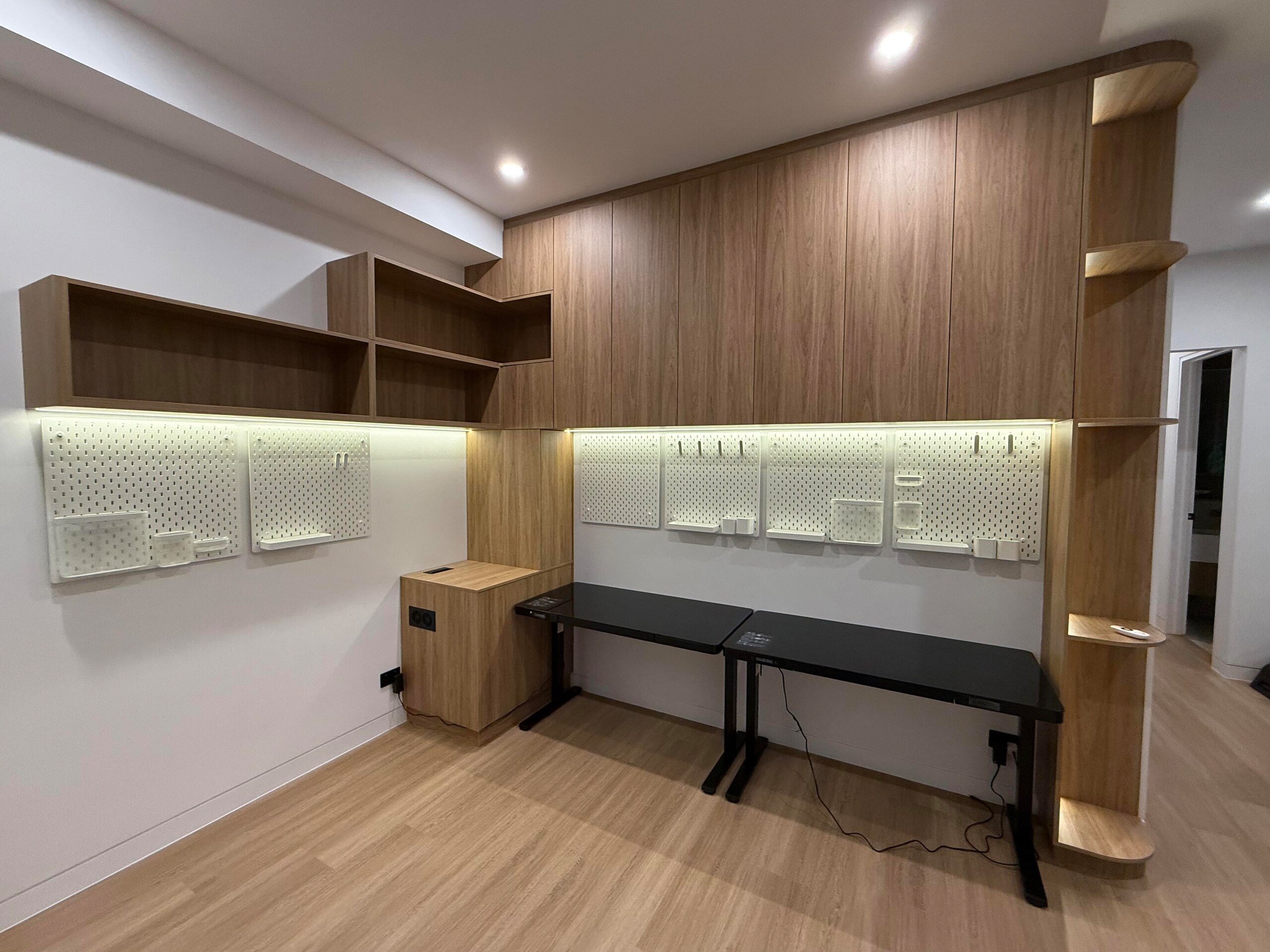 Home study with timber overhead cupboards, open shelves, a curved end shelf and lit pegboard over two desks