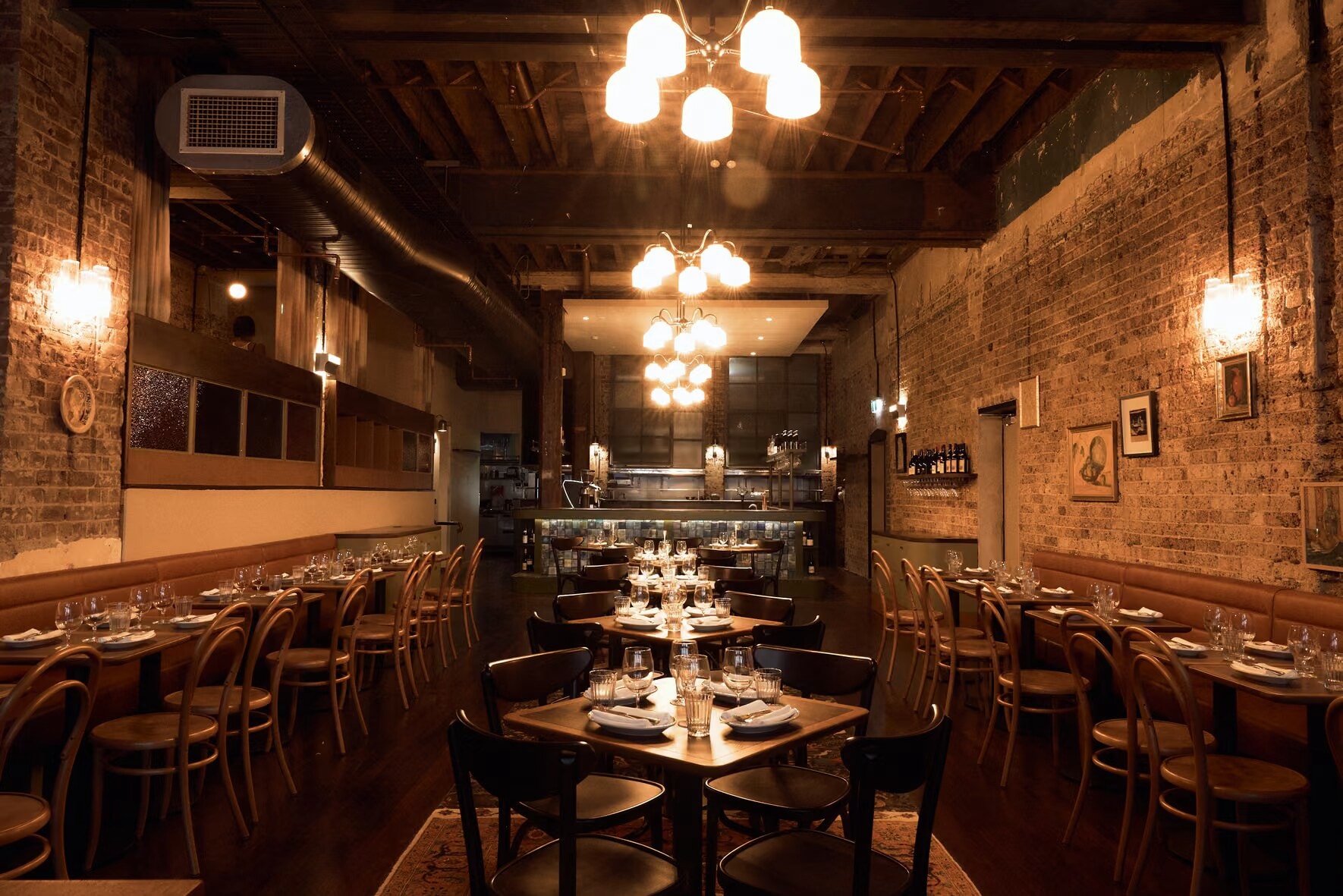Candle-lit dining room with chandeliers, banquettes and an open kitchen beyond