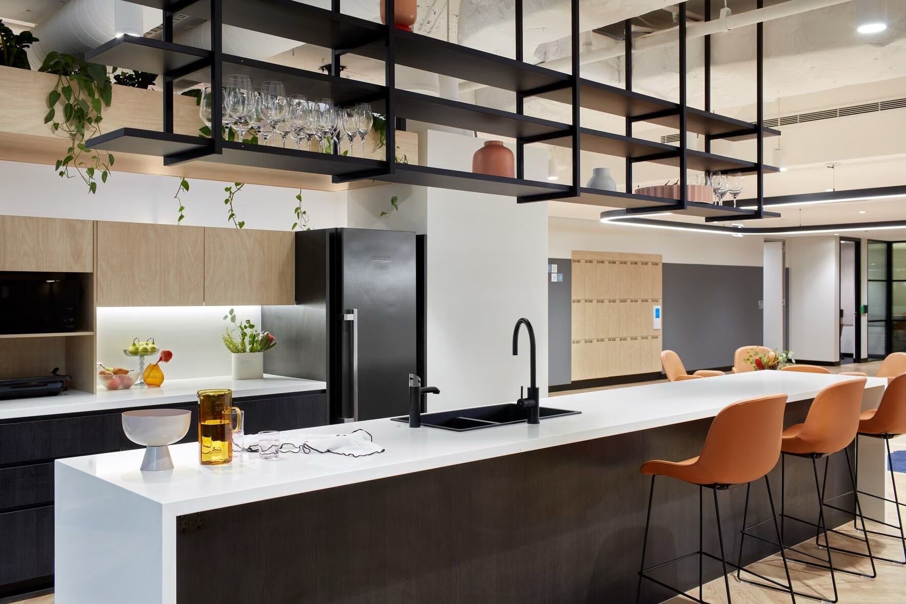 Office kitchen with a white island bench, dark cabinetry and a hanging shelf