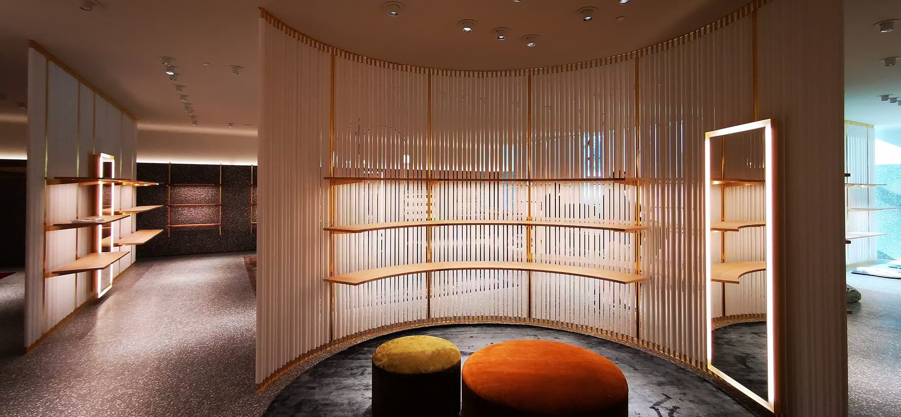 Curved fluted wall with brass shelves and velvet ottomans in a Valentino store