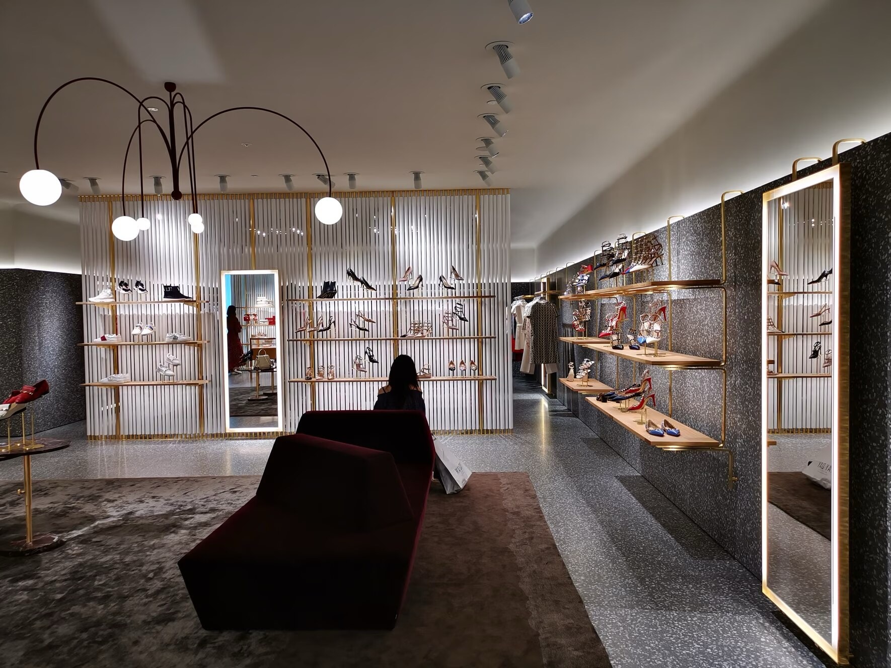 Valentino store shoe displays on brass shelving with a lit mirror