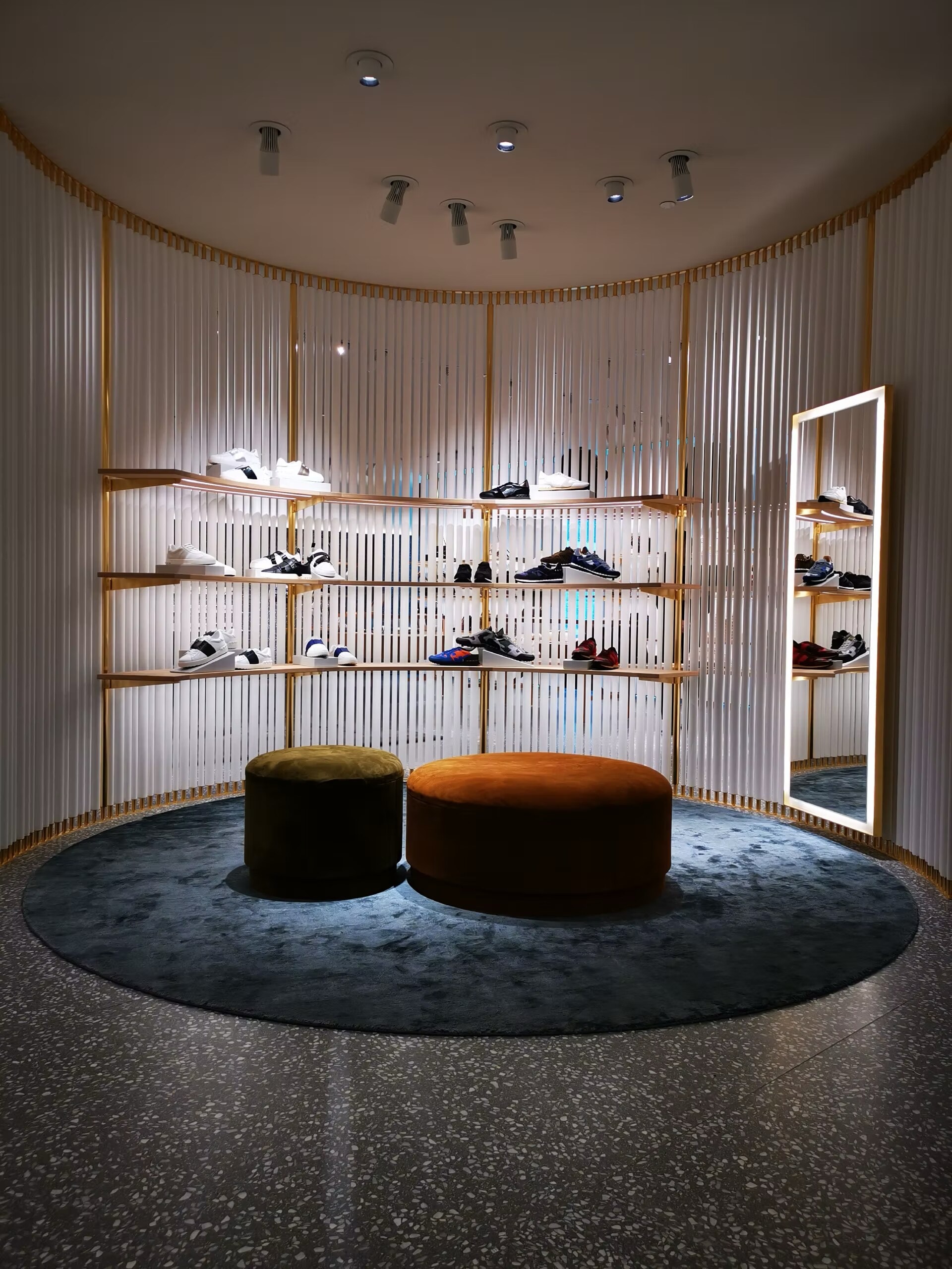 Valentino shoe room with curved fluted walls, brass shelves and ottomans