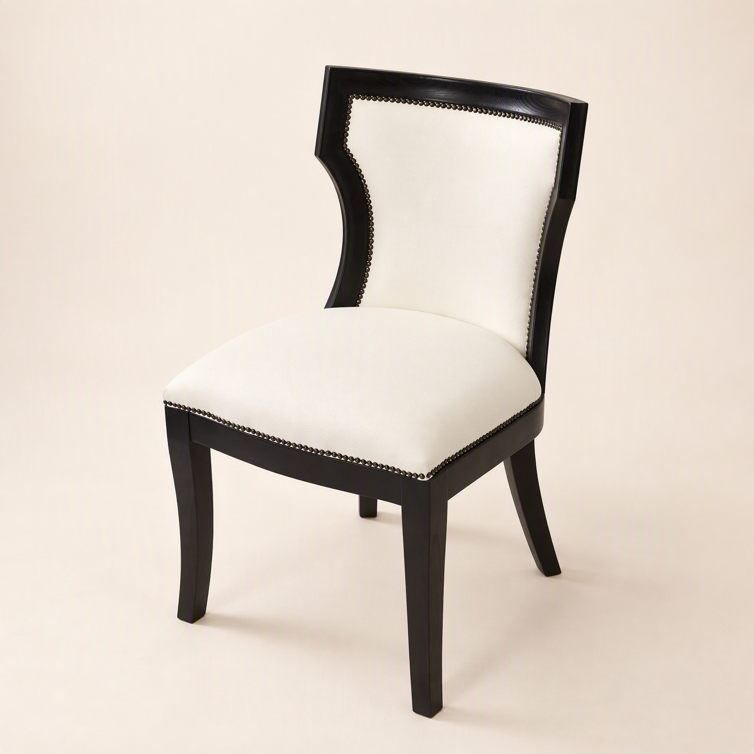A chair with a black curved timber frame, cream upholstery and stud trim